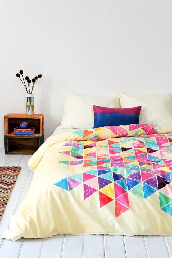 a neutral bedroom with a stained nightstand, a bed with colorful geometric bedding, a chevron rug and a geometric vase with dried blooms