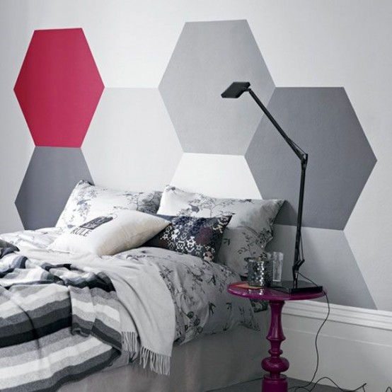 an eclectic bedroom with a grey, white and burgundy hexagon accent on the wall, a bed with grey and black dding, a burgundy nightstand with a black table lamp