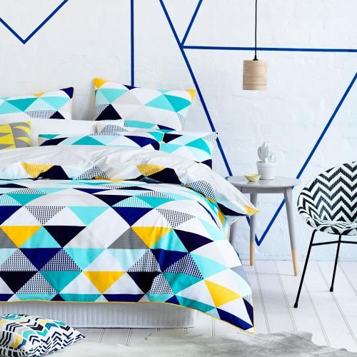 a bedroom with navy geo decor on the wall, a bed with colorful geo print bedding, a chevron print chair