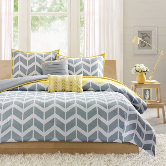 a neutral bedroom with a bed with grey and yellow geometric bedding, light-stained furniture, table lamps and neutral curtains