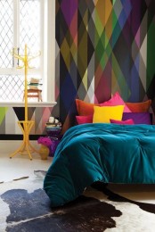 a colorful bedroom with a geometric accent wall, a bed with colorful bedding, a yellow rack, a purple nightstand, bright books