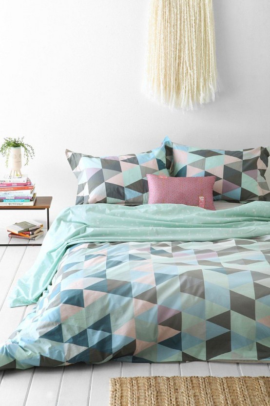 a neutral bedroom with a bed with geometric print bedding, a macrame hanging, a nightstand with greenery and books