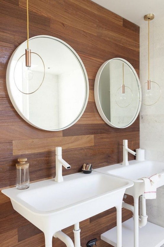 a chic mid-century modern bathroom with a wooden accent wall, white appliances and catchy pendant lamps over the sinks
