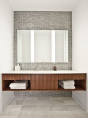 an elegant mid-century modern bathroom with grey tiles of various sizes and scales and a large floating vanity plus a statement mirror