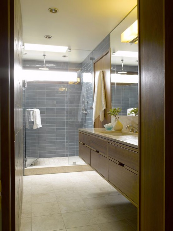 a stylish mid-century modern bathroom with blue tiles in the shower, neutral tiles on the floor and walls and a floating wooden vanity plus a large mirror