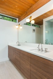an elegant mid-century modern bathroom with a stained wooden ceiling, a stained wooden vanity and all neutrals around plus a narrow skylight