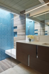 a stylish mid-century modern bathroom in neutrals, with a bold blue vertical tile wall, a dark stained floating vanity and a large lit up mirror