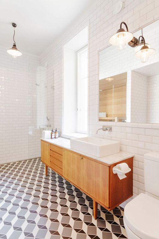 an airy mid century modern bathroom with mosaic tiles on the floor and white subway ones on the walls, a wooden vanity and mid century lamps