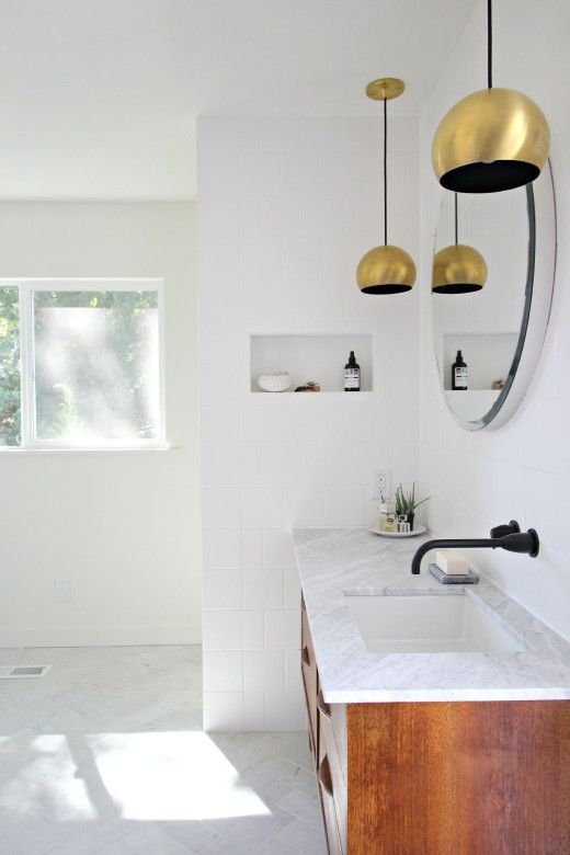 an elegant neutral mid-century modern bathroom with tiles and stone, a stained vanity and gold pendant lamps over the vanity