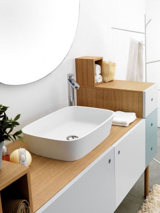 a neutral mid-century modern bathroom with a color block vanity, a round mirror and potted greenery