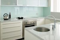 an airy white kitchen with white stone countertops, frosted glass cabinets and a mint glass backsplash is a lovely space