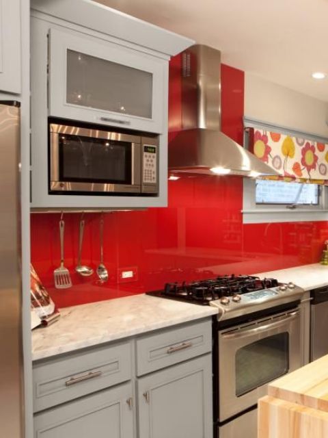 a pale blue kitchen with stainless steel touches, a bold red glass backsplash and a bold floral curtain for a touch of color