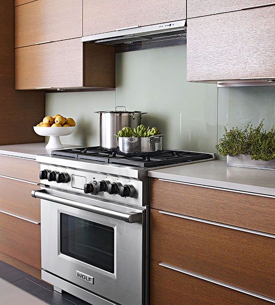 a rich-stained modern kitchen with stainless steel touches, white stone countertops and a light grene solid glass backsplash for a sleek touch