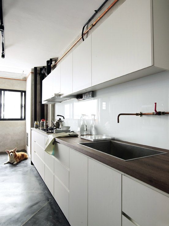 a modern white kitchen with sleek cabinets, dark stained butcherblock countertops and a white solid glass backsplash
