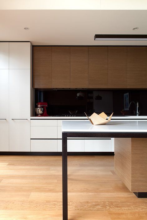 a two-tone kitchen with dark-stained and white cabinets, white countertops and a black glass backsplash to add a bit of drama to the space