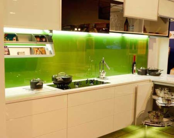 a modern white kitchen with sleek white cabinets, a bold green glass lit up backsplash for a touch of color and a more modern feel