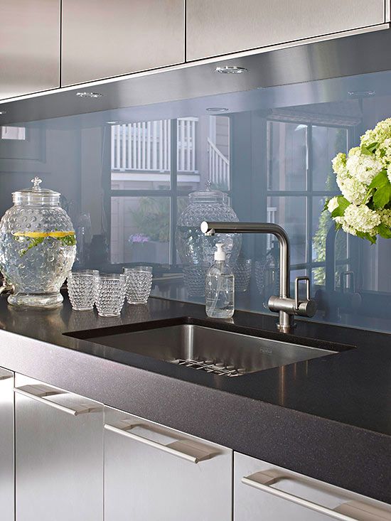 a stainless steel kitchen with black countertops and a blue glass backsplash for a super modern and bold look