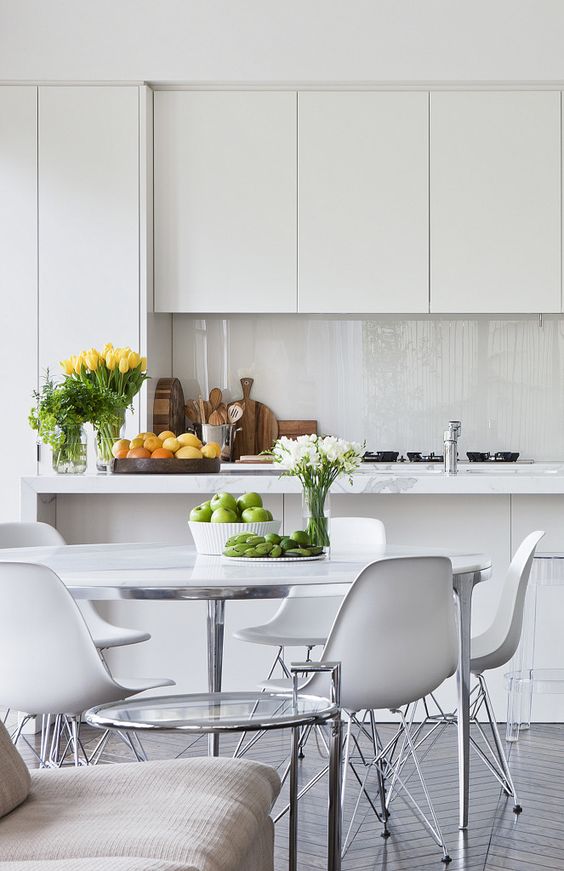 a minimalist white kitchen with sleek cabinets with no handles, a glossy white glass backsplash and white stone countertops