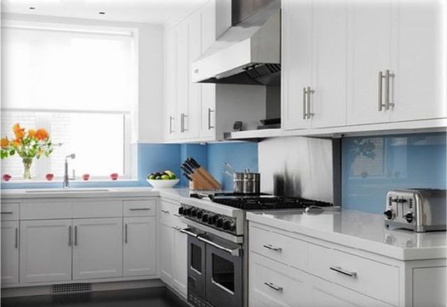 a modern white kitchen with shaker cabinets, white stone countertops and a blue glass backsplash for a touch of gloss and color