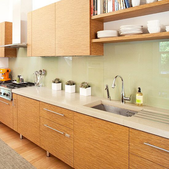 a modern light-stained kitchen with neutral stone countertops, a neutral solid glass backsplash and laconic fixtures is a chic and stylish space
