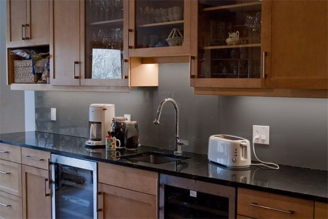 a light-stained modern kitchen with shaker cabinets, black stone countertops and a grey solid glass backsplash is a chic space