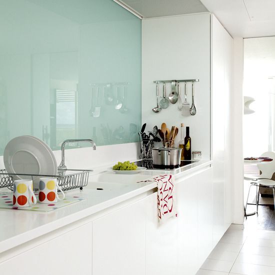 a minimalist white kitchen with white stone countertops and a mint glass backsplash is a stylish and catchy space in soft shades