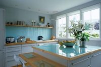 a modern white kitchen with a solid blue glass backsplash and a matching countertop plus light-stained wooden touches is an airy and chic space