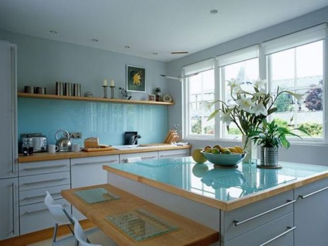 a modern white kitchen with a solid blue glass backsplash and a matching countertop plus light-stained wooden touches is an airy and chic space