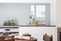 a minimalist white kitchen with sleek cabinets, dark countertops, a grey glossy glass backsplash for a soft touch of color