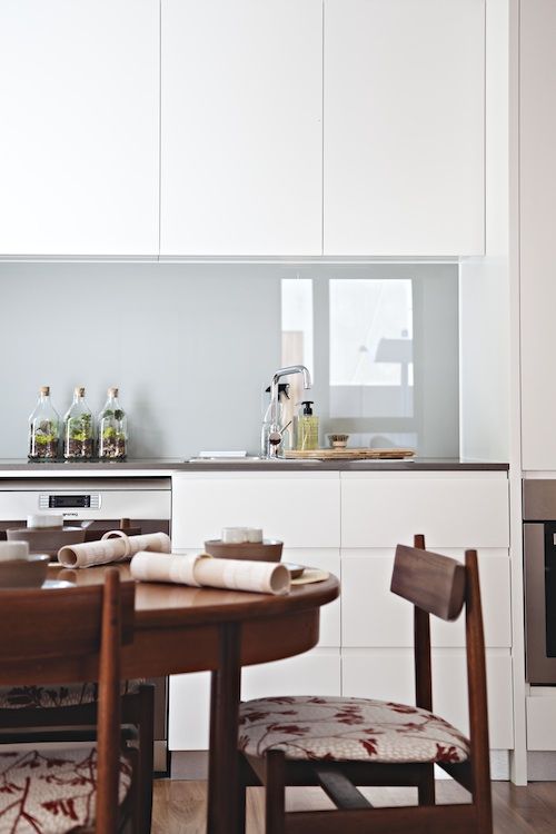 a minimalist white kitchen with sleek cabinets, dark countertops, a grey glossy glass backsplash for a soft touch of color