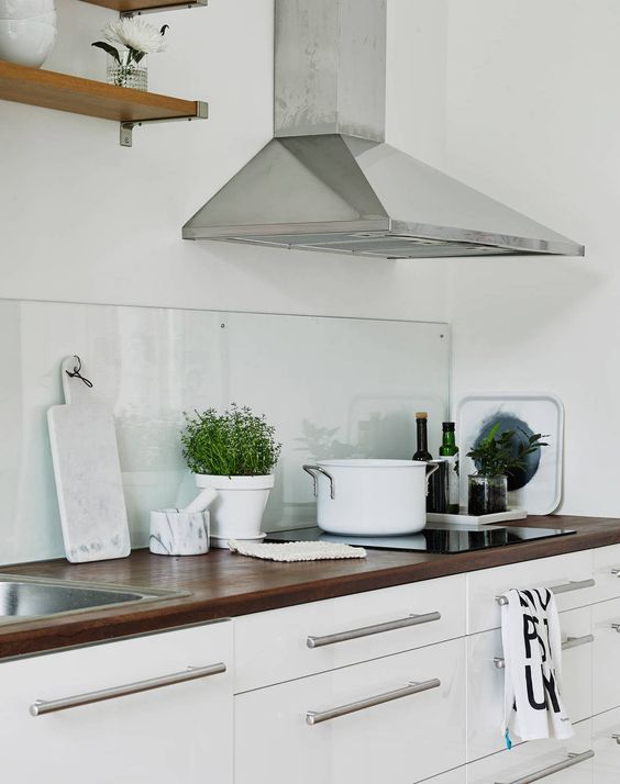 a white Scandinavian kitchen with dark-stained butcherblock countertops and a clear glass backsplash that helps to create a calm feel