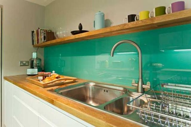 a modern white kitchen with light-stained butcherblock countertops and a bold green glass backsplash that contrasts the cabinets
