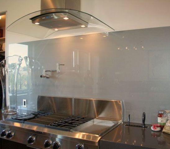 a black kitchen with stainless steel appliances and a glossy grey glass backsplash for a soft and delicate touch of color and a shiny feel