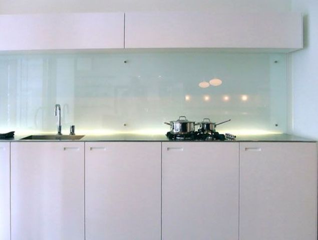 a sleek modern white kitchen with a dark countertop and a light blue solid glass backsplash that is a subtle touch of color