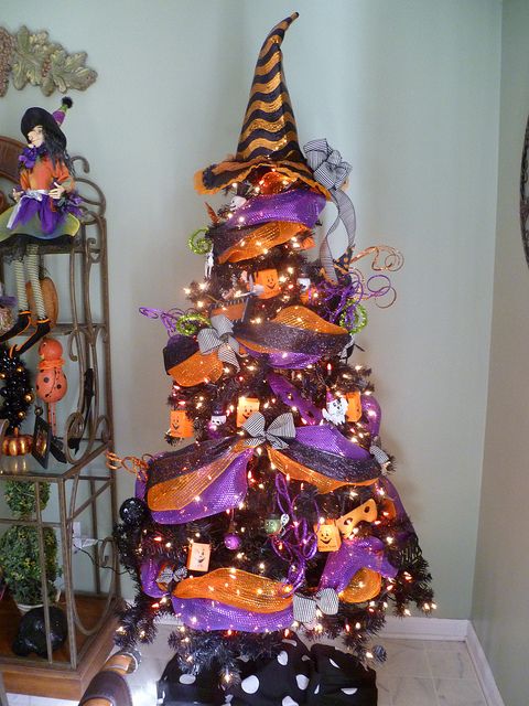 a black Halloween tree decorated with purple and orange ribbons, lights, wooden ornaments and a witch hat on top