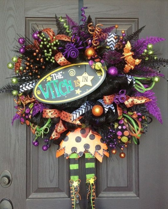 a super colorful Halloween wreath in orange, purple and green, with ribbons, berries, ornaments and witches' hats and legs