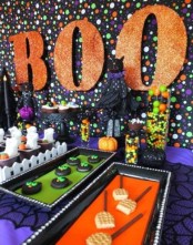 bright Halloween dessert table styling with a polka dot backdrop, orange glitter letters, bold sweets and candies on bold trays for a kids’ party