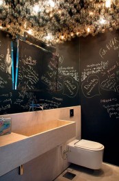 a contemporary bathroom with black chalkboard walls, a light stone vanity with a built-in sink, a mirror and some bulbs on the ceiling
