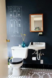 a modern bathroom with black chalkboard walls, a tiled floor, a toilet and a wall-mounted sink and a mirror