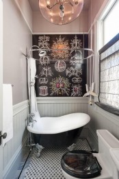 a vintage bathroom with grey walls and white paneling, a black vintage tub, a black chalkboard wall with images and some curtains