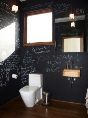 a modern chalkboard bathroom with a small window, a wall-mounted sink, a mirror and a toilet plus some writing on the walls