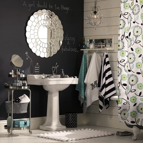 a farmhouse bathroom with a chalkboard and a white shiplap wall, a pedestal sink, a round mirror, some printed textiles