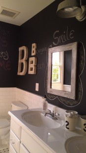 a farmhouse bathroom with black chalkboard walls, white tiles, a white vanity and a sink, a mirror and a gallery wall