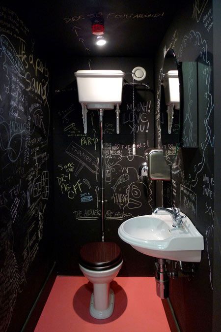 a catchy and bold powder room with black chalkboard walls, a wall mounted sink, a toilet and a red floor plus some red touches