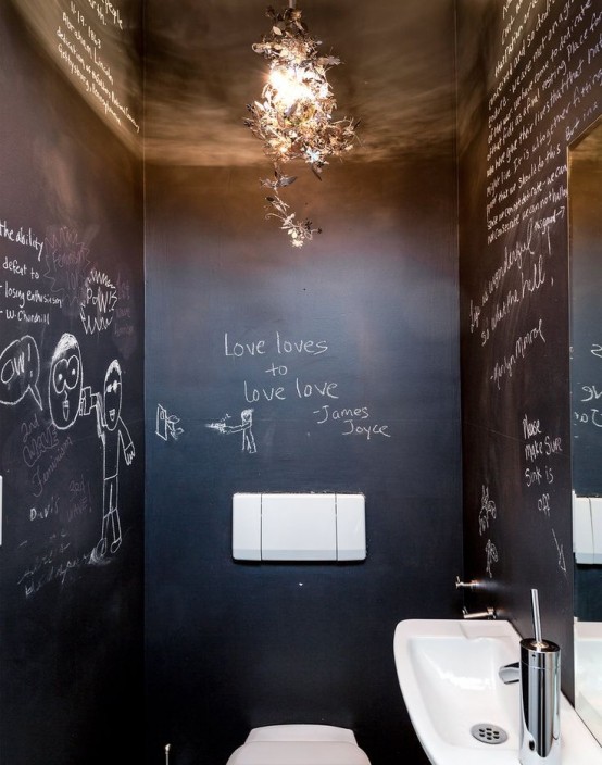 a small modern powder room with black chalkboard walls, a wall-mounted sink,a toilet and a chandelier plus a catchy chandelier