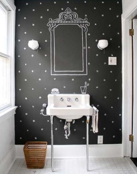 a black and white bathroom with a black chalkboard accent wall and a chalked mirror and decor, a sink on a stand, a basket and some sconces is a cool and modern space