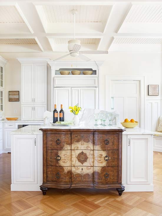 a white kitchen island with storage compartments and a vintage stained dresser integrated into the island looks really unusual