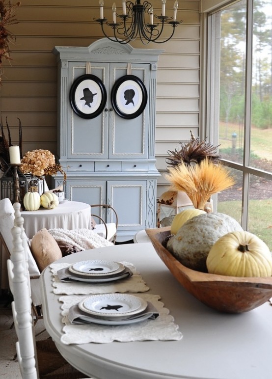 a neutral vintage and rustic Thanksgiving tablescape with lace placemats, printed plates, a wooden bowl with wheat and neutral pumpkins