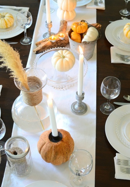 a vintage Thanksgiving tablescape with a brown tablecloth and neutral linens, white candles, natural pumpkins, wheat and driftwood candleholders