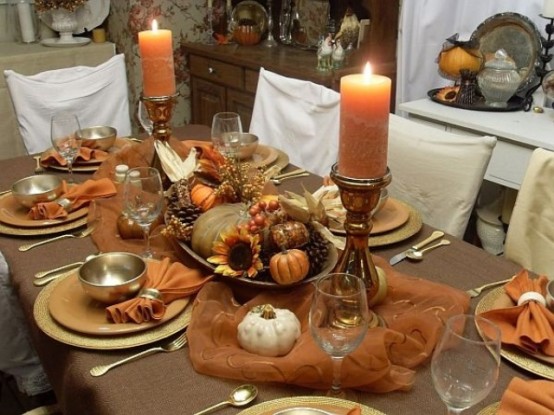a vintage Thanksgiving tablescape done in brown and rust, with metal chargers, metallic and neutral pumpkins, pinecones, rust candles in candleholders, shiny gold plates and cutlery